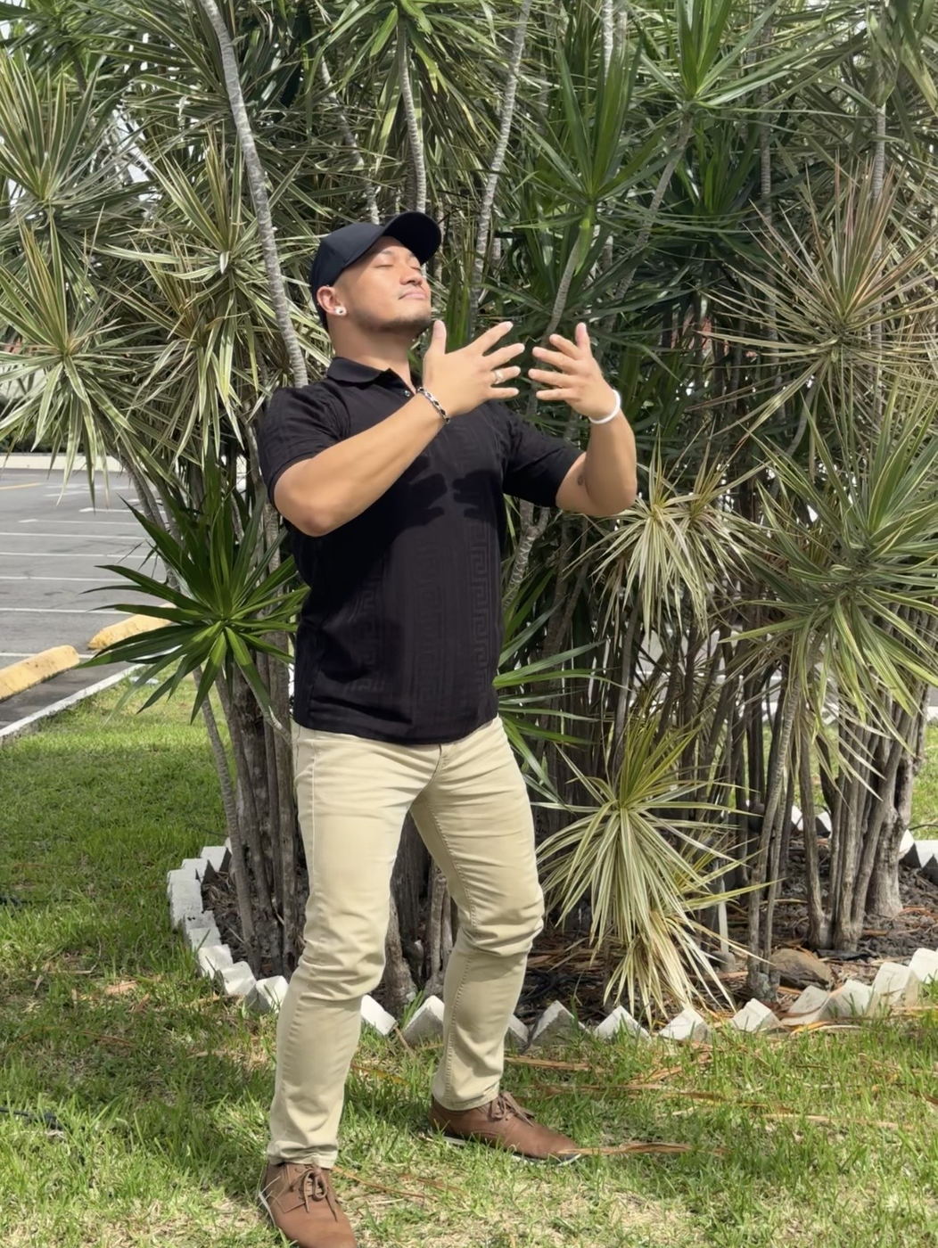 Zano holding a qigong posture outdoors, hands raised and eyes closed.